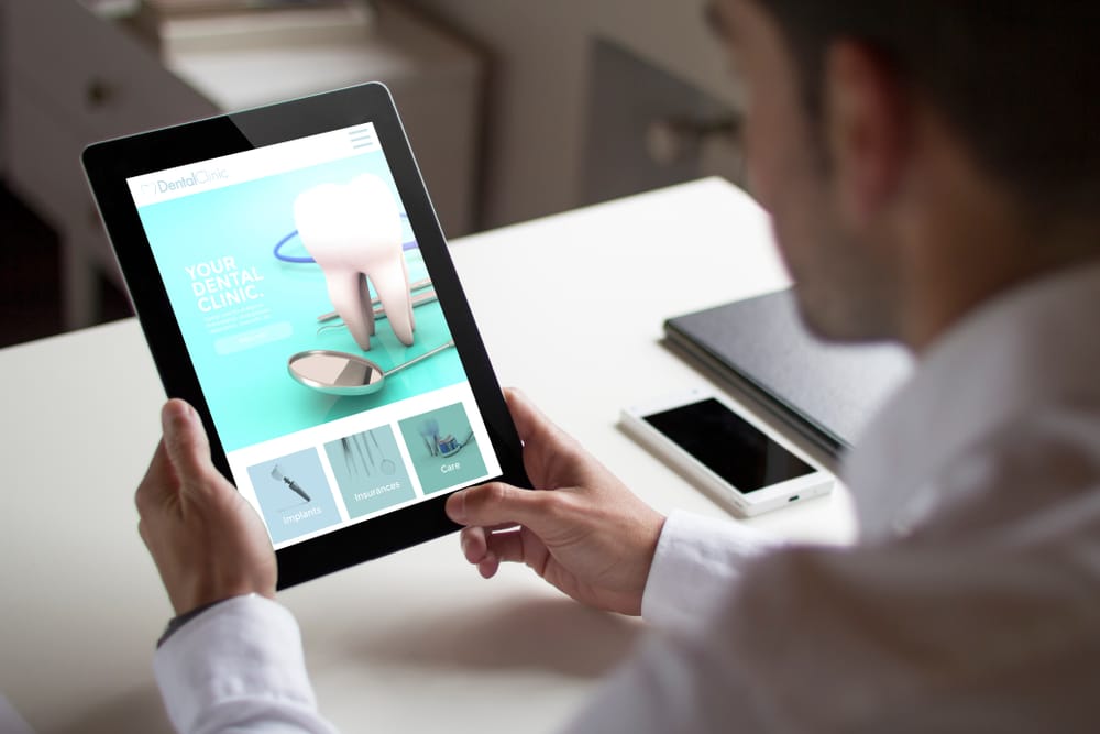 Bussinessman,At,Office,Holding,A,Tablet,Showing,Dental,Clinic,Website.